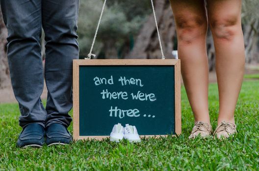 Feet of father and mother with baby shoes and a black slate, concept for the baby's welcome