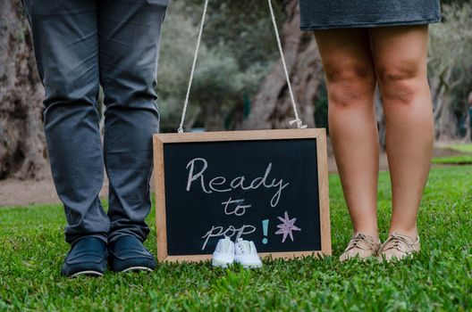 Feet of father and mother with baby shoes and a black slate, concept for the baby's welcome