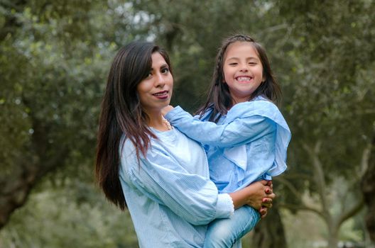 Mother carrying her cute and smiling daughter in the park on a winter afternoon