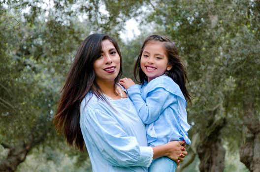 Mother carrying her cute and smiling daughter in the park on a winter afternoon