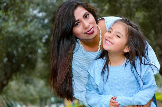 Mother carrying her cute and smiling daughter in the park on a winter afternoon