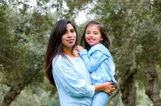 Mother carrying her cute and smiling daughter in the park on a winter afternoon