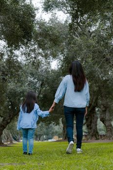 Mother and little Peruvian girl walking together on an autumn afternoon, seen from the back