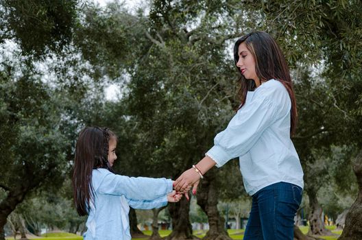 Mother and little daughter holding hands having fun in a park on a nice winter day.