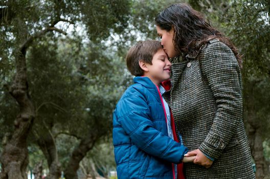 Portrait of a mother kissing her little son in the park a winter day