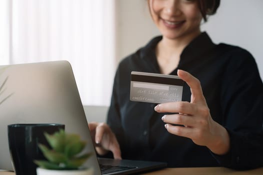 Young woman holding credit card and using laptop computer at home. Online shopping, e-commerce, internet banking, spending money