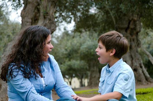 Beautiful woman and her cute little son looking to each other amazed in the park