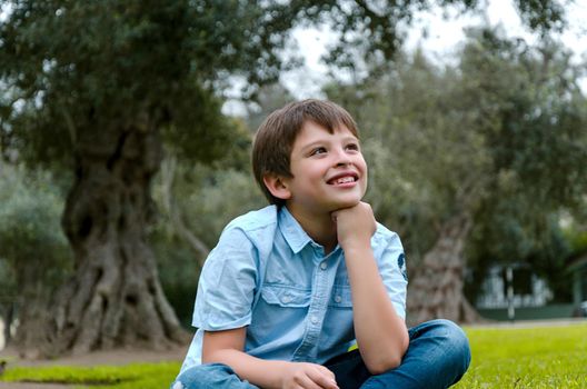 Cute little boy sitting in the park smiling thinking about something