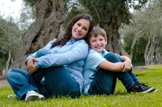 Mom and son sitting on green grass in green park. Concept of happy family relations and carefree leisure time