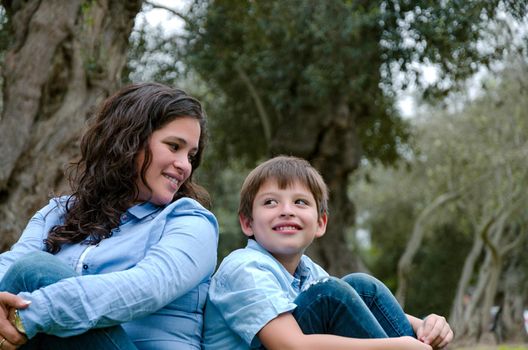 Mom and son sitting on green grass in green park. Concept of happy family relations and carefree leisure time