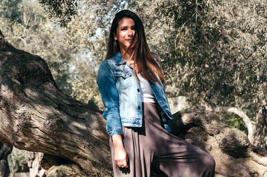 Beautiful long-haired teen woman with brown hair leaning on a tree in the park