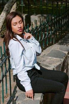 Brunette woman sitting on the bench with park background and smile to camera