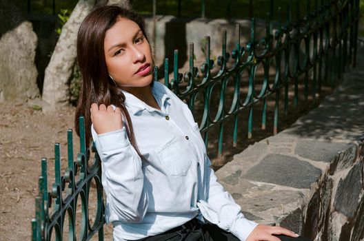 Brunette woman sitting on the bench with park background and smile to camera