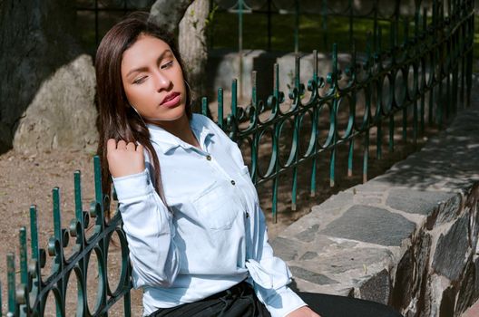 Brunette woman sitting on the bench with park background and smile to camera