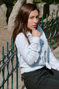 Brunette woman sitting on the bench with park background and smile to camera