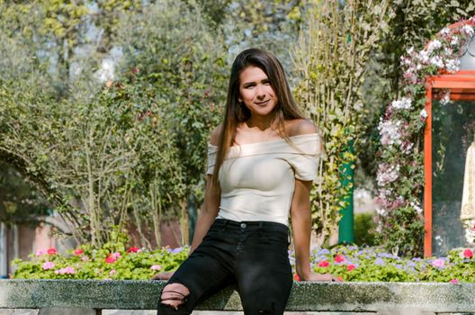 Happy young woman sitting on bench in city park Stylish fashion model wearing ripped jeans and pullover