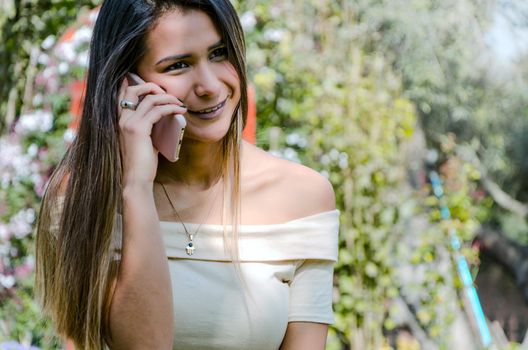 Beautiful young smiling woman talking on cell phone with green background of a park