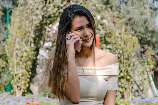 Beautiful young smiling woman talking on cell phone with green background of a park