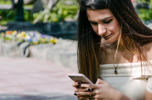 Happy girl watching media in a smartphone sitting on a bench of a city park