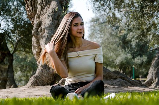 Beautiful brunette woman touching her long hair. She sits in a park on green grass. The image is toned.