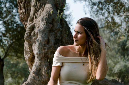 Beautiful brunette woman touching her long hair. She sits in a park on green grass. The image is toned.
