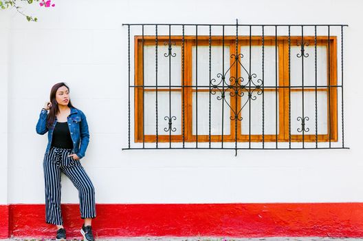 Stylish young woman posing against window outdoors. Fashionable outfit. Beautiful model smiling