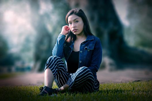 Portrait of an attractive, young and attractive brunette woman sitting on the lawn. She leans back and relaxes while smiling.