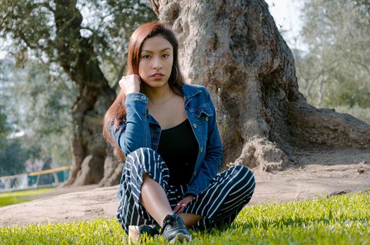 Portrait of an attractive, young and attractive brunette woman sitting on the lawn. She leans back and relaxes while smiling.