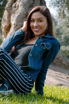 Portrait of an attractive, young and attractive brunette woman sitting on the lawn. She leans back and relaxes while smiling.