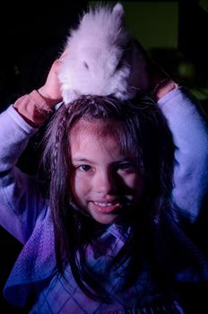 Happy little girl with her pet bunny on her head on dark background