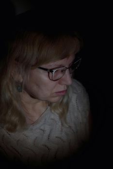 Face portrait of an aged woman wearing glasses with white long curly hair. Black background