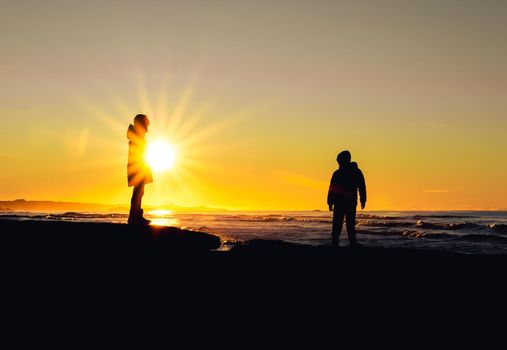 Two kids playing with each other at the beach while the sun is setting. Temperature is just below zero, but with sunny day and no wind it makes for a lovely evening at the beach.