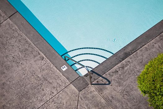 Corner of emerald swimming pool with steps leading to the deeper water and metal rail on side