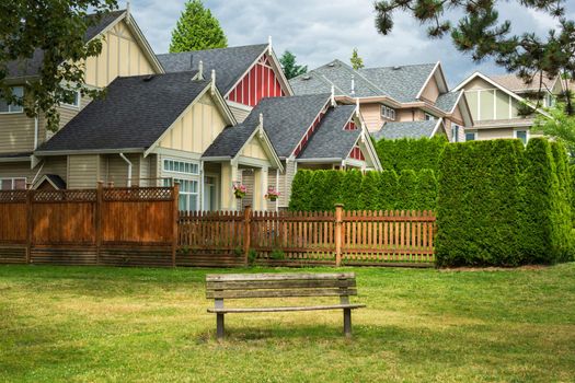 Old wooden bench in a park are in front of residential houses.