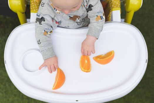 Cute little baby eating orange sitting in the high chair.