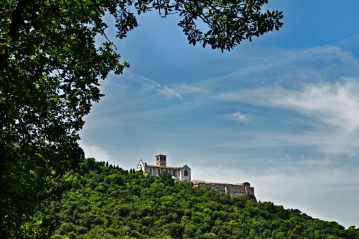 Assisi ,Italy , Basilica of Saint Francis and Sacro Convento  as seen from the wood of Saint Francis below , the Basilica  between the blue sky and the beautiful wood