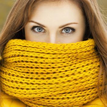 Pretty woman in a yellow knit scarf looking at the camera. Beautiful eyes peering.