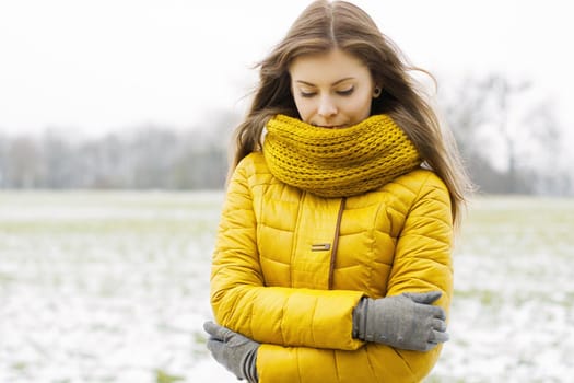 Pretty woman in a yellow knit scarf and yellow jacket. Outdoors portrait in the park.