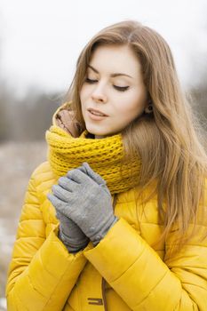 Pretty woman in a yellow knit scarf. Warm hands. Looking down.