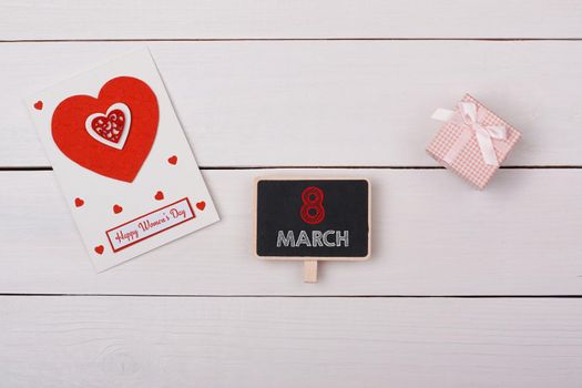 Blackboard with 8 march tag, a gift and a card with red hearts on a white table.