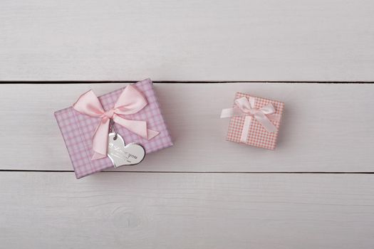 Two pink gifts with bows on white wooden table.