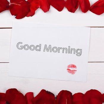 Sheet of paper Good Morning with a kiss. Note and rose petals on the table