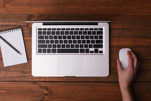 Desk with a laptop, a notebook with a pencil. Female hand holding a mouse.