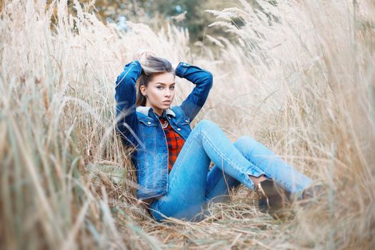 Stylish fashionable girl in jeans clothes in the autumn field.