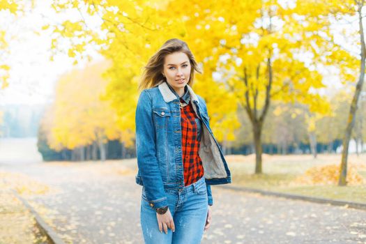 Pretty girl in jeans clothes and a red checkered shirt in autumn park.