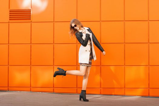 Pretty fashion woman in dress and sunglasses.Background of a bright orange wall.