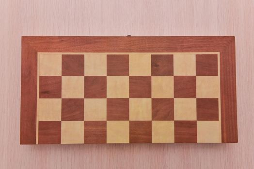 Top view on wooden chess board on light wooden table background.