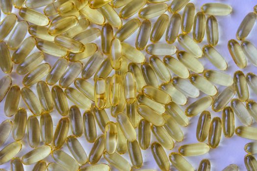 Bunch of omega 3 fish liver oil capsules in pile. Close up of big golden translucent pills texture. Healthy every day nutritional supplement. Top view.