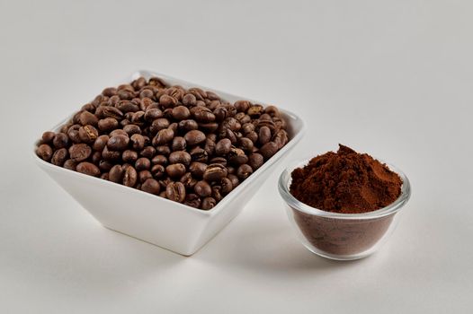 Roasted whole peaberry coffee beans and freshly ground coffee powder on a white background