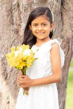 Little girl in white dress and with a cute bouquet of flowers in her hand